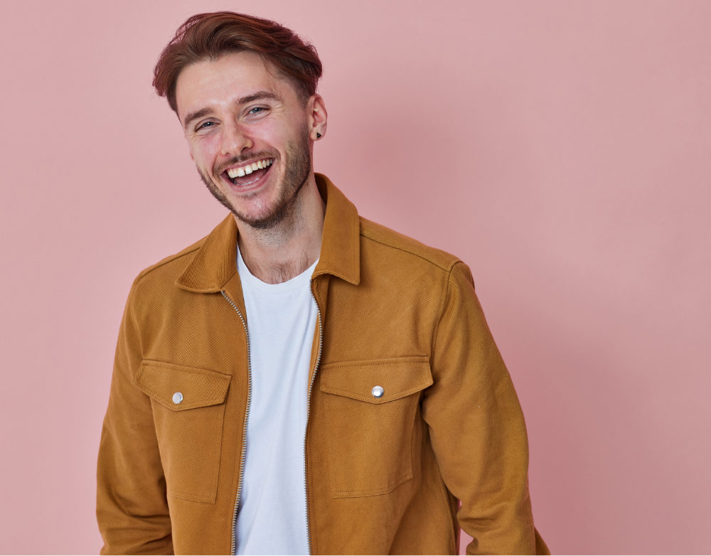 young man in a yellow jacket smilng on a pink background
